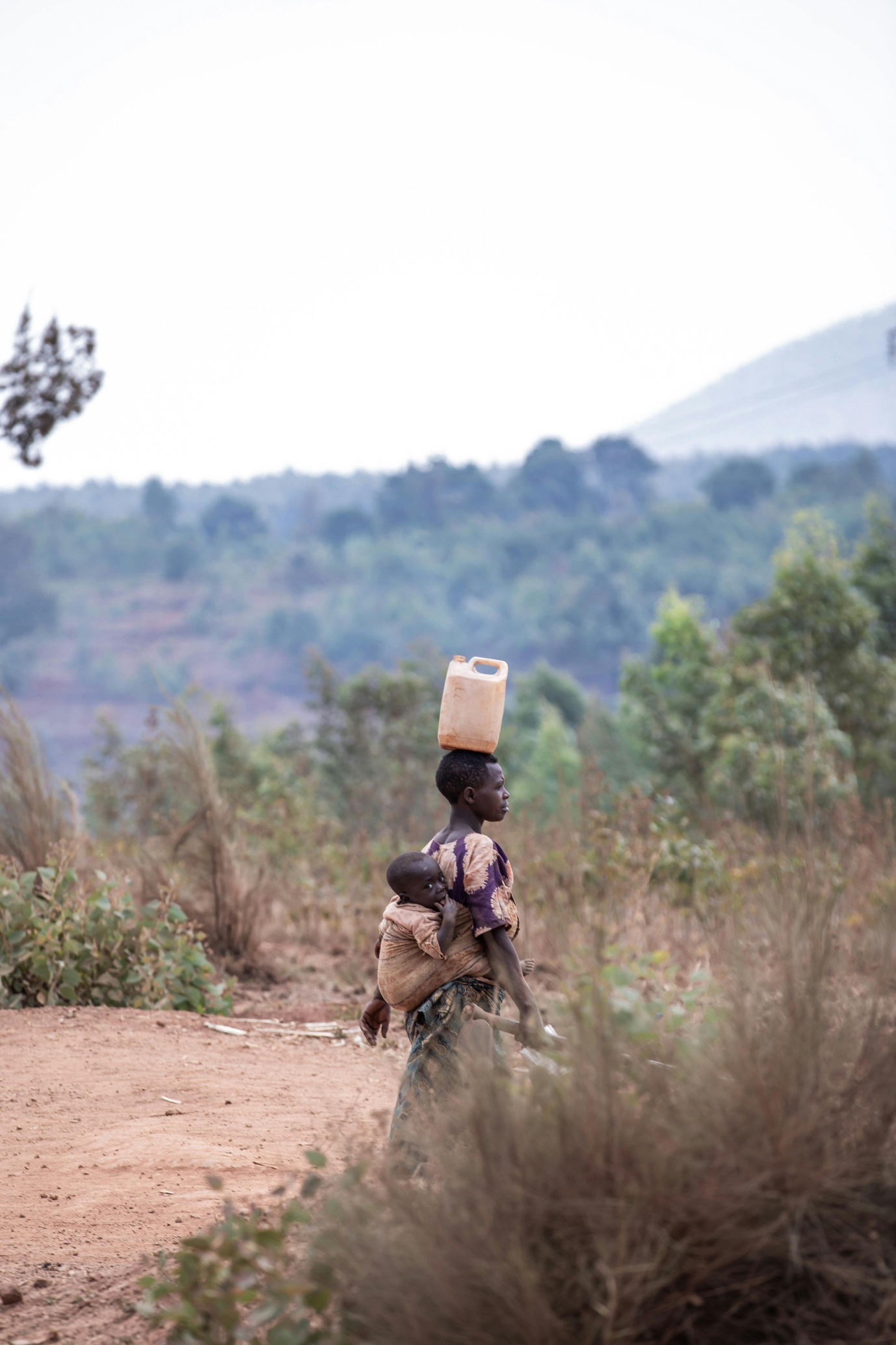 A person carrying a baby on her backDescription automatically generated